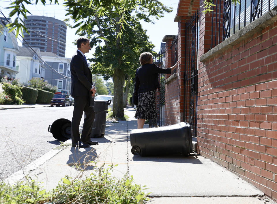 Carrie Sideris rings a doorbell as her husband Dan Sideris looks on as the couple returns to door-to-door visits as Jehovah's Witnesses, Thursday, Sept. 1, 2022, in Boston. (AP Photo/Mary Schwalm)