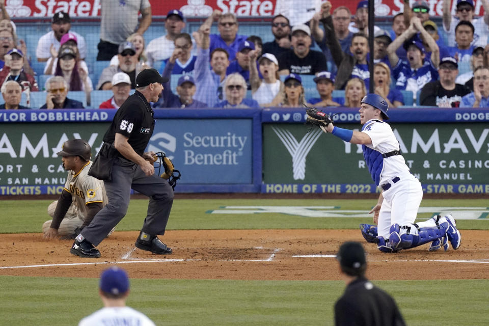 San Diego Padres' Trent Grisham, left, sits after being tagged out by Los Angeles Dodgers catcher Will Smith, right, as he tried to score from third after Jurickson Profar lined out as home plate umpire Dan Iassogna makes the call during the second inning of a baseball game Thursday, June 30, 2022, in Los Angeles. (AP Photo/Mark J. Terrill)