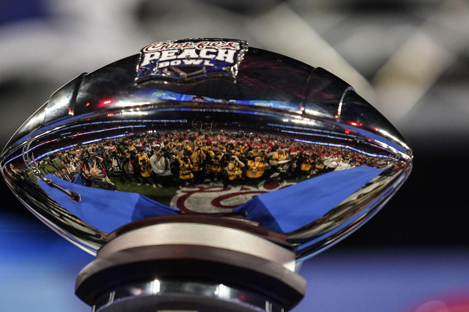 Photographers are reflected in the The George P. Crumbley Trophy after the Peach Bowl NCAA college football semifinal playoff game between Georgia and Ohio State, Sunday, Jan. 1, 2023, in Atlanta. Georgia won 42-41. (AP Photo/Brynn Anderson)