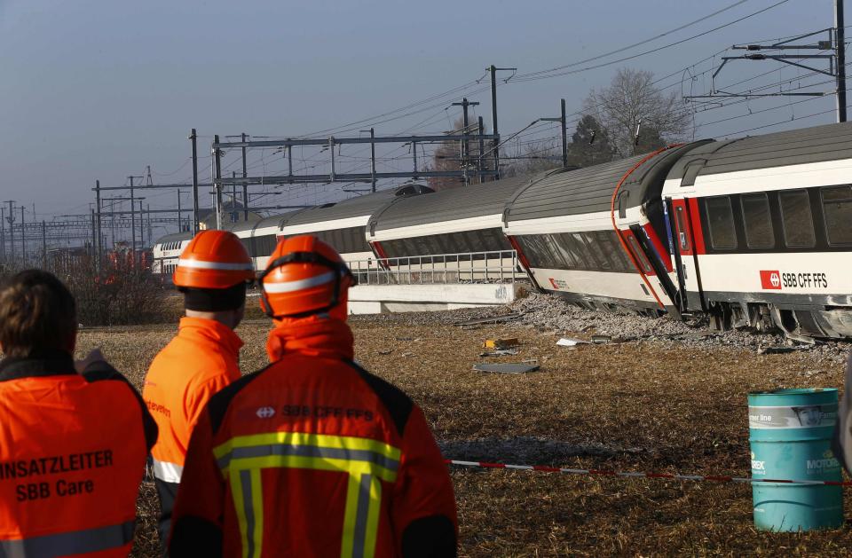 Rescue workers stand next to a derailed train after two trains collided near Rafz