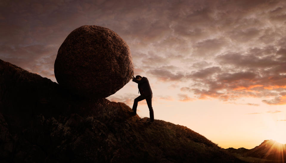 Man in a business suit pushing a boulder up a hill