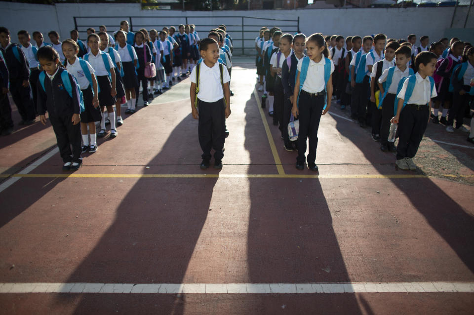 In this Oct. 2, 2019 photo, children line up for their first day of school in Caracas, Venezuela. The school year began amid the once-wealthy country's deepening crisis, with more teachers and students abandoning their homeland, leaving classrooms empty. Those remaining behind say they struggle to afford basic school supplies, some deciding not to attend at all, which experts say puts the next generation's chance for success in jeopardy. (AP Photo/Ariana Cubillos)