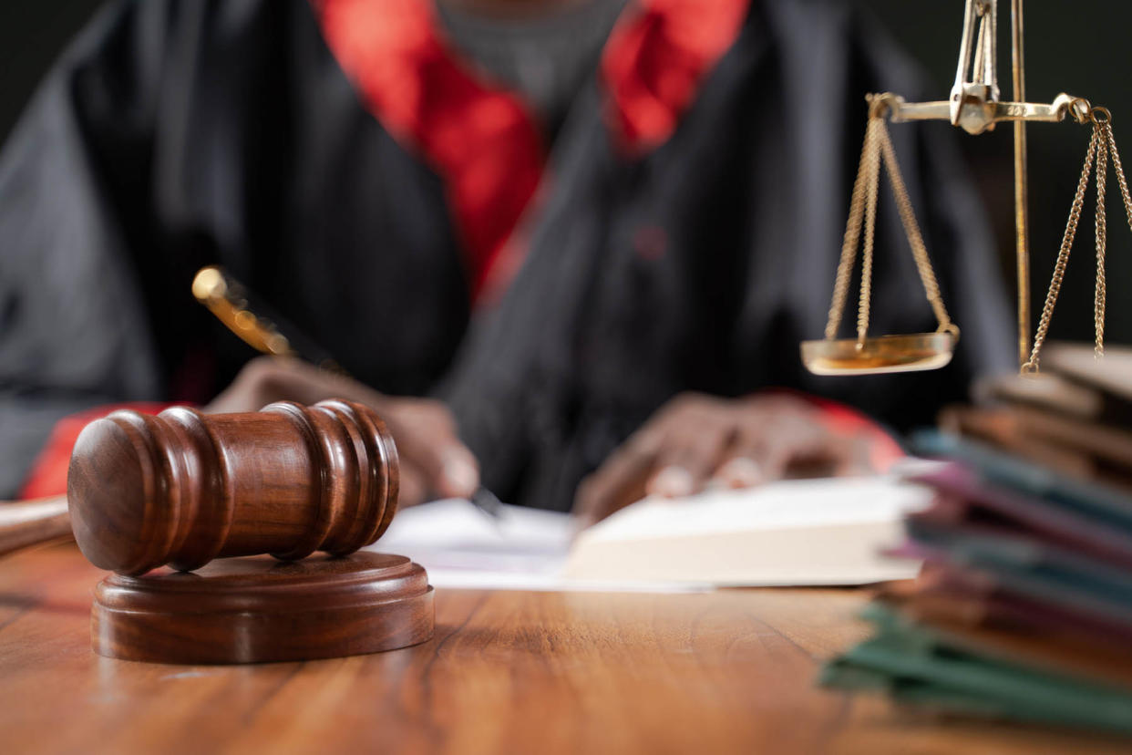 Focus on judge gavel, Unrecognizable judge busy writing verdict or making notes from the book with gavel and balance scale on table. - Credit: iStockphoto/Getty Images