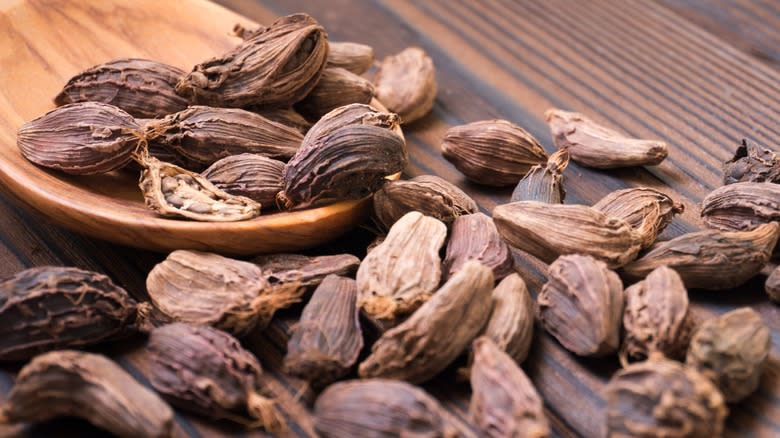 Black cardamom seeds spilling out of a wooden spoon