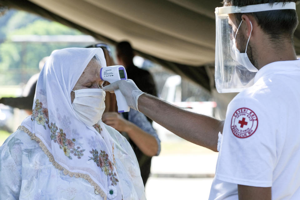 A health worker measures the temperature of a woman before granting her access to the memorial cemetery in Potocari, near Srebrenica, Bosnia, Saturday, July 11, 2020. Nine newly found and identified men and boys were laid to rest as Bosnians commemorate 25 years since more than 8,000 Bosnian Muslims perished in 10 days of slaughter, after Srebrenica was overrun by Bosnian Serb forces during the closing months of the country's 1992-95 fratricidal war, in Europe's worst post-WWII massacre. (AP Photo/Kemal Softic)