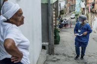 A resident stands in her doorway as a member of the "Bora Testar" or Let's Test project, walks through the the Paraisopolis neighborhood of Sao Paulo, Brazil, Friday, Sept. 11, 2020. The project plans to test up to 600 people for COVID-19 in the low income neighborhood, and to expand to other vulnerable communities in the country, financed by crowdfunding and donations. (AP Photo/Carla Carniel)