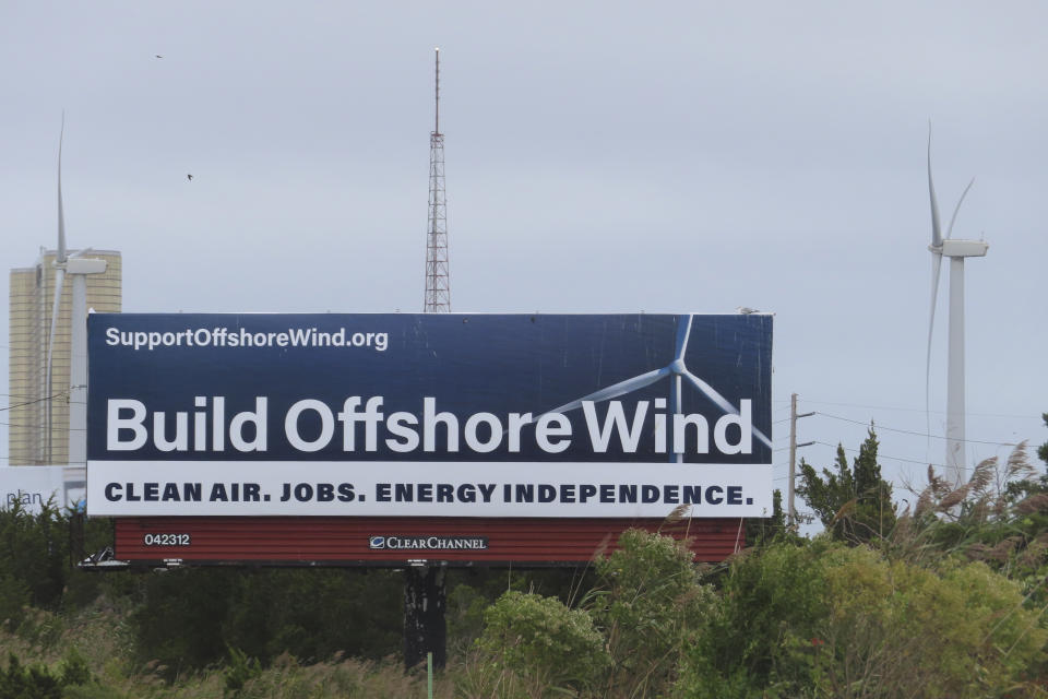 A billboard supporting offshore wind power projects sits on a roadside near land-based wind turbines in Atlantic City, N.J., on Wednesday, Sept. 18, 2024. (AP Photo/Wayne Parry)