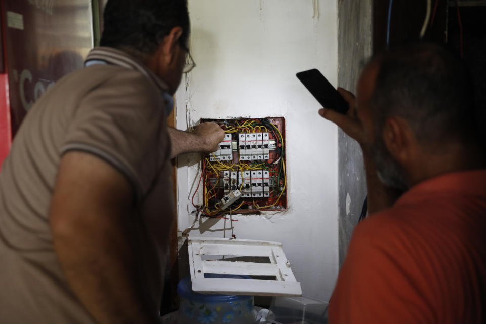 A Lebanese man, right, lights by his mobile phone for an electrician worker, left, who sets an electricity switch for a coffeeshop from a private-owned generators that provide power to homes and businesses, after the power remains shut off about 20 hours a day in Beirut, Lebanon, Wednesday, July 29, 2020. The multiple crises may seem like a standard summer in Lebanon, a country constantly vaulting from one disaster to the other. Only this time they come on top of financial ruin, collapsing institutions, hyperinflation and rapidly rising levels of poverty and unemployment. (AP Photo/Hussein Malla)