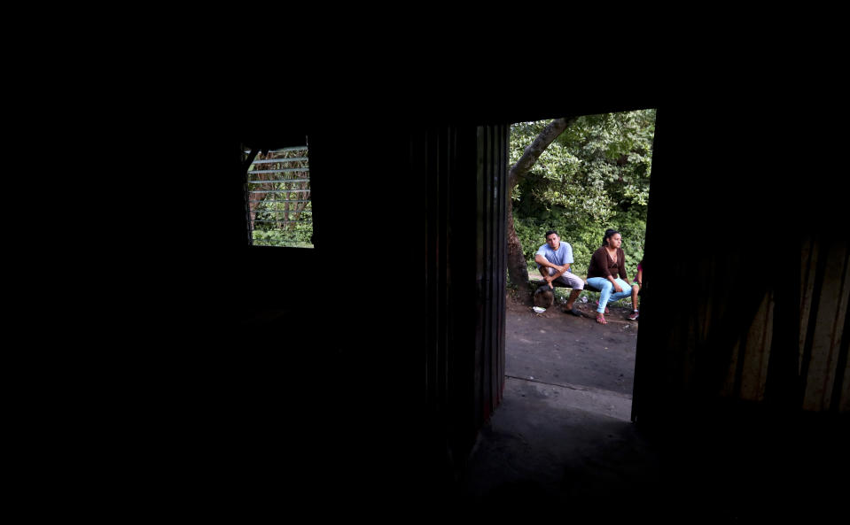 In this Oct. 12, 2019 photo, members of a family sit outside their makeshift house, after being threatened by gangs in Oratorio de Concepcion, El Salvador. The family had to leave their home, carrying only what they were wearing and taking refuge in this place. (AP Photo/Eduardo Verdugo)