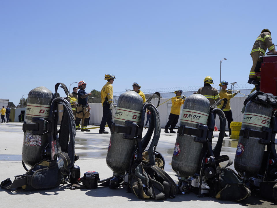 Cadets, who were formerly-incarcerated firefighters, load a fire hose onto a fire truck after using Self Contained Breathing Apparatuses, SCBA, foreground, at the Ventura Training Center (VTC) during an open house media demonstration Thursday, July 14, 2022, in Camarillo, Calif. California has a first-in-the nation law and a $30 million training program both aimed at trying to help former inmate firefighters turn pro after they are released from prison. The 18-month program is run by Cal Fire, the California Conservation Corps, the state corrections department and the nonprofit Anti-Recidivism Coalition at the Ventura Training Center northwest of Los Angeles. (AP Photo/Damian Dovarganes)