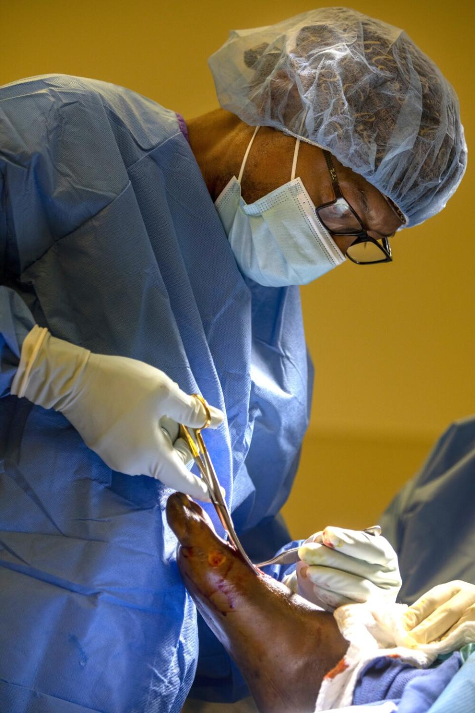 A surgeon uses instruments to work on a patient's bare foot.