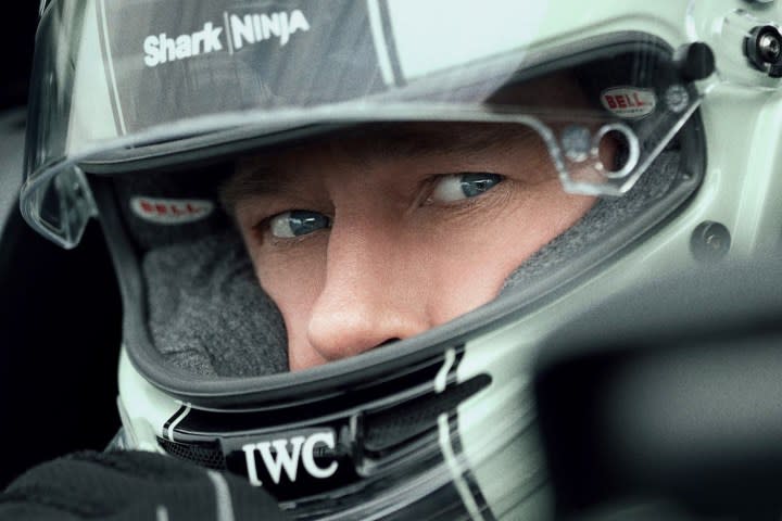 Brad Pitt sits in the front seat of a car with a racing helmet.