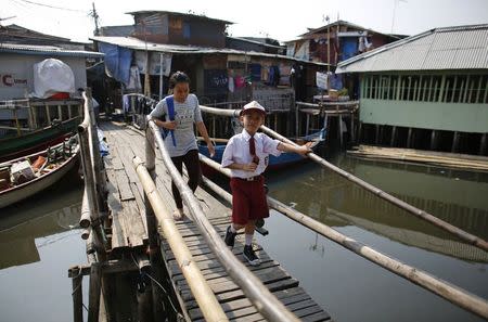 A school boy crosses a bridge in Luar Batang, one of the oldest kampongs in Jakarta, dating back to the16th century, in north Jakarta September 30, 2014. REUTERS/Darren Whiteside
