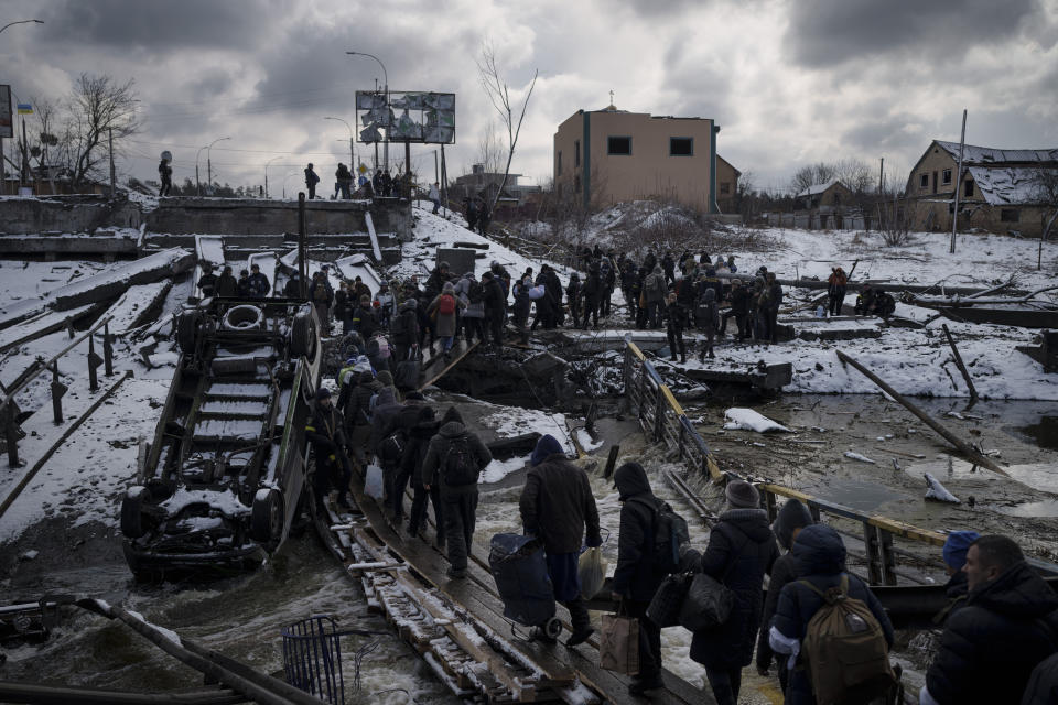 ARCHIVO - Ucranianos cruzan un puente improvisado bajo un puente roto mientras huyen de Irpin, a las afueras de Kiev, Ucrania, el martes 8 de marzo de 2022. Como hito, el primer aniversario de la invasión rusa en Ucrania es tan sombrío como exasperante. Es un año repleto de muerte, destrucción, pérdida y daños que se sienten mucho más allá de las fronteras de Rusia y Ucrania. (AP Foto/Felipe Dana, Archivo)