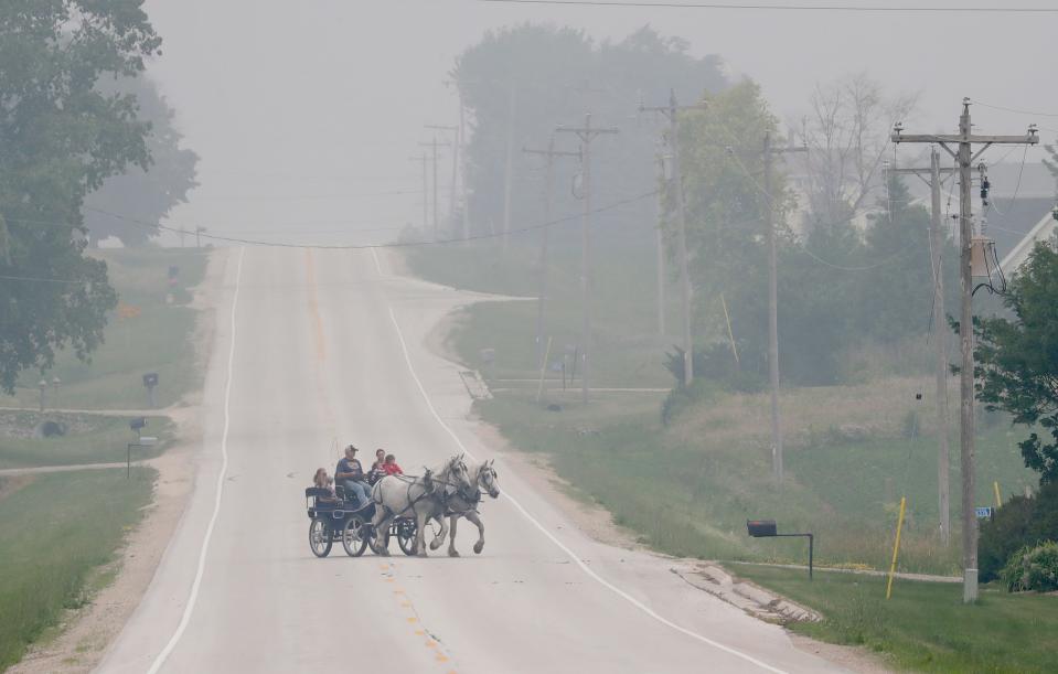 Under hazy skies, John and Jenny Petrie take their grandchildren and daughter-in-law Katie Petrie for a horse and carriage ride Tuesday, June 27, 2023, along County BB in the Town of Chilton, Wis.