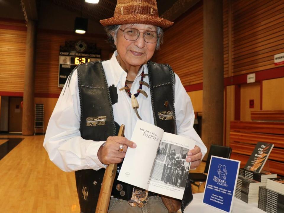 Squamish Elder Sam George holds a copy of his memoir The Fire Still Burns: Life In and After Residential School at an event launching its publication in North Vancouver, B.C., on Saturday. (Chad Pawson/CBC News - image credit)