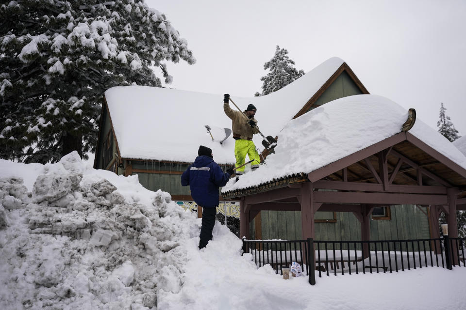Kevin Maze, top, and Donnie Smith remove snow from a structure in Running Springs , Calif., Tuesday, Feb. 28, 2023. Beleaguered Californians got hit again Tuesday as a new winter storm moved into the already drenched and snow-plastered state, with blizzard warnings blanketing the Sierra Nevada and forecasters warning residents that any travel was dangerous. (AP Photo/Jae C. Hong)