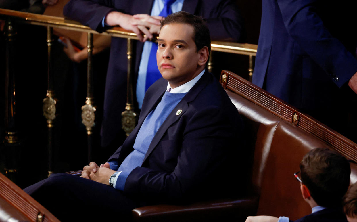 Rep. George Santos sits in his leather House seat, looking up warily at the camera.