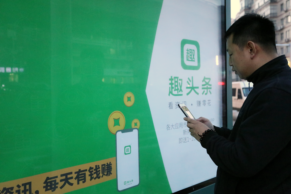 Mobile user in front a Qutoutiao sign.