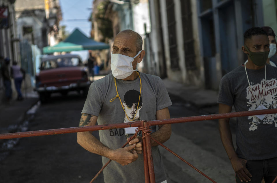 Hombres montan guardia en una reja que corta el acceso a su vecindario para mantener alejados a los que no viven allí, como una forma de frenar la propagación de COVID-19 en La Habana, Cuba, el lunes 22 de febrero de 2021. (AP Foto/Ramon Espinosa)