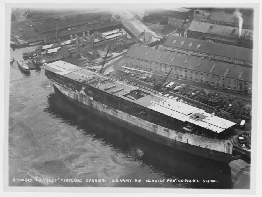 Under reconstruction from the collier JUPITER at Norfolk Navy Yard, Portsmouth, Virginia, circa late 1921. Note boat storage yard ashore, and USS GEORGE E. BADGER (DD-196) in background. (NHHC)