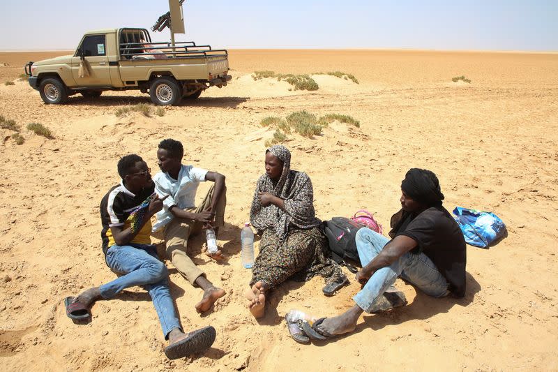 Tafaul Omar, a pregnant 26-year-old nurse from Sudan, talks to a group of men as she is stranded in the desert on the Libyan-Tunisian border, near Al-Assah