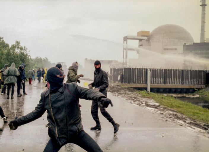 FILE - Hooded violent demonstrators hurl rocks towards police water cannons behind the security fence surrounding the nuclear power plant in Brokdorf, Germany, June 7, 1986. Germany on Friday, Dec. 31, 2021 is shutting down half of the six nuclear plants it still has in operation, a year before the country draws the final curtain on its decades-long use of atomic power. (AP Photo/Heribert Proepper, file)