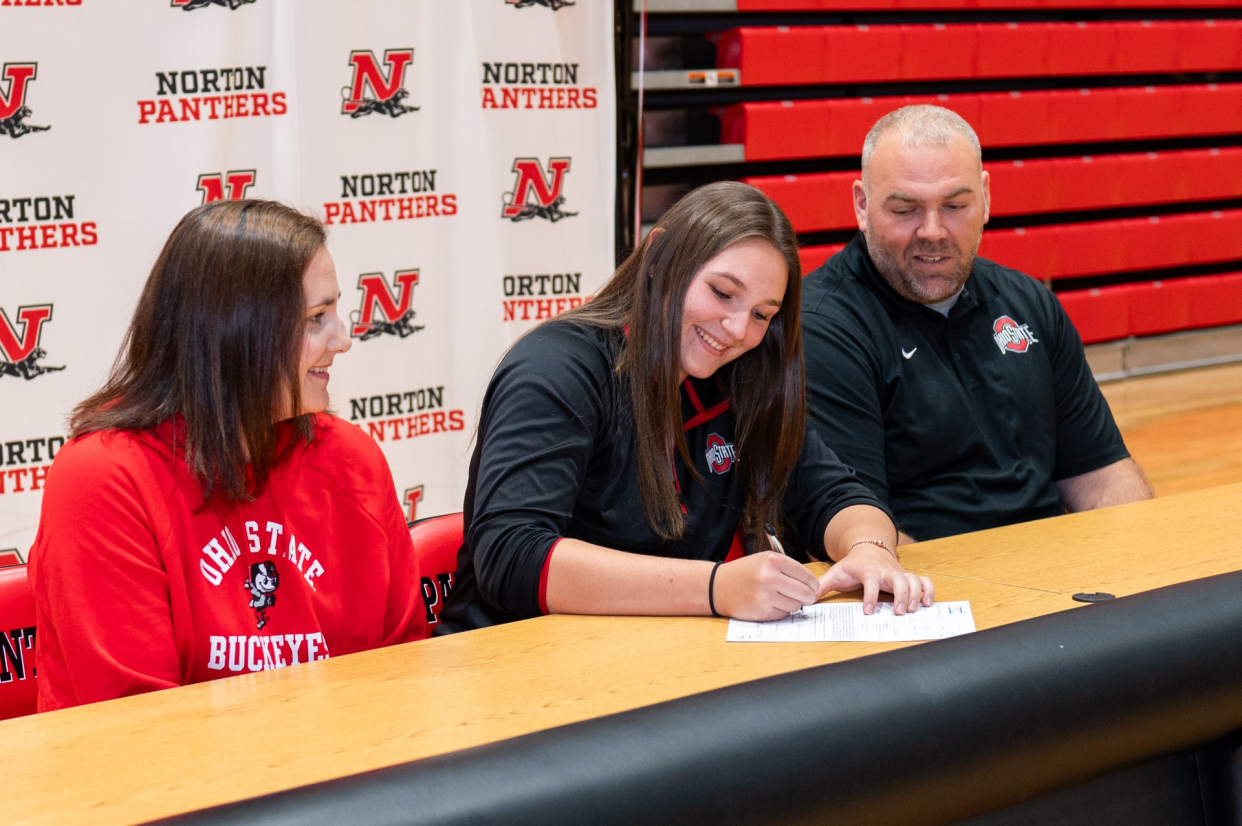 Norton High School senior Morgan Hallett, center, signs a national letter of intent to continue her track and field career at Ohio State University with her her parents, Jennifer and Brian, at her side on Wednesday, Nov. 8, 2023.