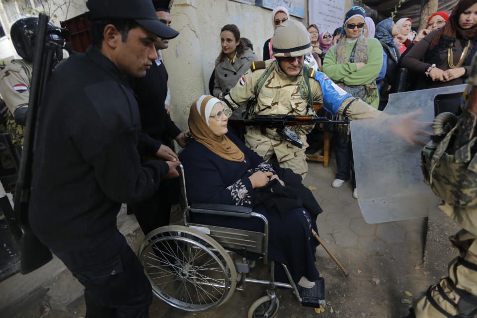 An Egyptian army soldier and policemen, left, help an elderly woman on a wheelchair in front of a polling station in Cairo, Egypt, Tuesday, Jan. 14, 2014. Egyptians are voting Tuesday on a draft for their country's new constitution that represents a key milestone in a military-backed roadmap put in place after President Mohammed Morsi was overthrown in a popularly backed coup last July. (AP Photo/Amr Nabil)