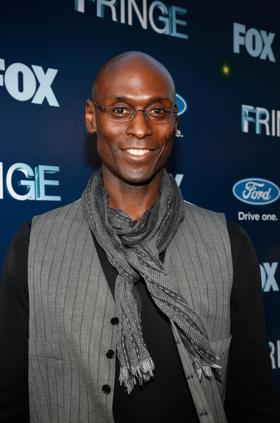 lance reddick wearing a gray shirt and scarf and glasses