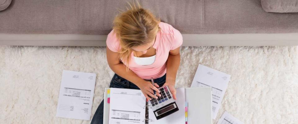 High Angle View Of A Woman Sitting On Carpet Calculating Invoice Using Calculator At Home