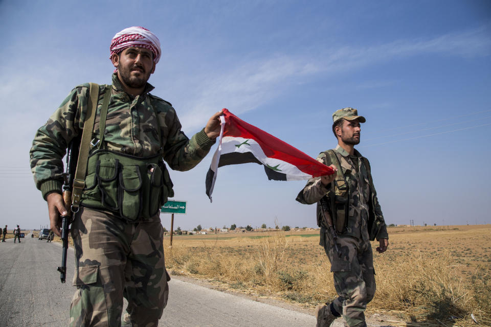 FILE - Syrian government forces carry a national flag as they walk at a checkpoint near the town of Tal Tamr, north Syria, on Oct. 22, 2019. For years, Syria’s civil war has been a largely frozen conflict, the country effectively carved up into areas controlled by the Damascus government of President Bashar Assad, various opposition groups and Syrian Kurdish forces. But as the conflict entered its 14th year on Friday, March 15, 2024 observers say violence has been on the rise again while the world’s attention is mostly focused on other crises, such as Russia’s onslaught on Ukraine and the Israel-Hamas war in Gaza. (AP Photo/Baderkhan Ahmad, File)