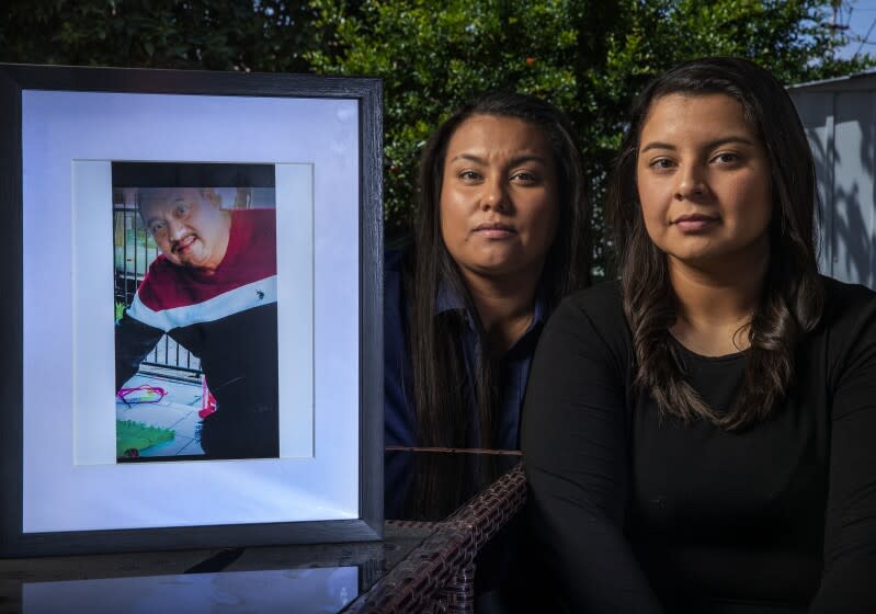 NORWALK, CA-MAY 27, 2022: Johanna Garcia, 27, left, and her sister Katherine Garcia, 21, are photographed at their home in Norwalk. They are the daughters of Enrique Garcia, seen in framed photograph, a 49 year old Santa Ana man and forklift operator who died in December of 2017 after a medical procedure at South Coast Global Medical Center. The Garcia sisters sued a gastroenterologist for negligence but lost at trial last moth on Orange County civil court. After the verdict, Robert McKenna III, an attorney representing the doctor, appeared in a social-media post celebrating the verdict in a way that sparked controversy. (Mel Melcon / Los Angeles Times)