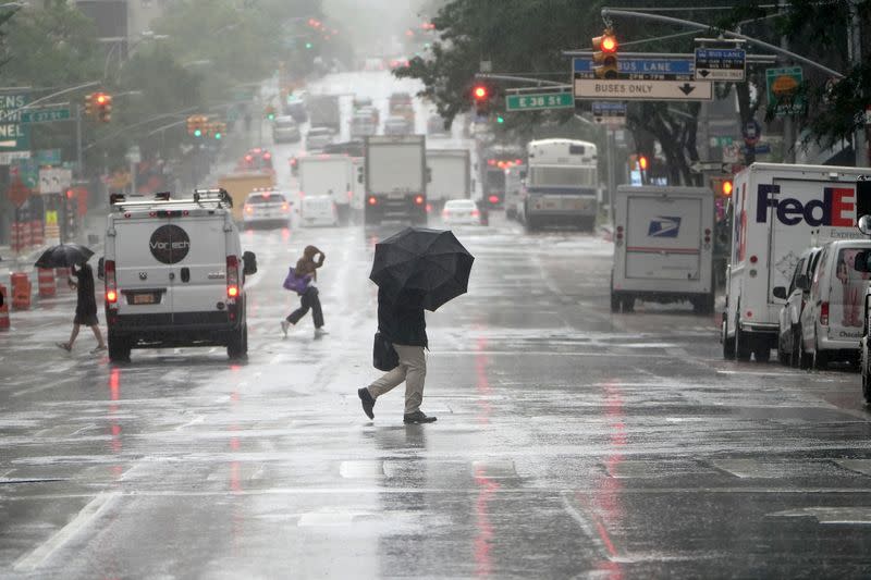 People with umbrellas cross a street as the city starts to feel the effects of Tropical Storm Isaias