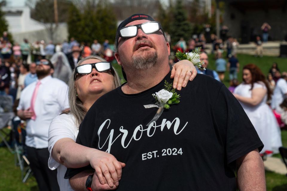 Cynthia Caldwell, of Columbus, Ohio, holds onto her husband, Robert Caldwell, of Columbus, while watching with others as the solar eclipse nears totality while waiting with others to get married during the Elope at the Eclipse event at the Frost Kalnow Amphitheater in Tiffin, Ohio on Monday, April 8, 2024. Over 100 couples and their families gathered to be married or renew their vows during the totality of the eclipse event.
