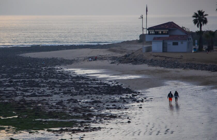 TOPANGA STATE BEACH, CA - December 06 2021: A couple walk along the beach at low tide as the sun sets on Monday, Dec. 6, 2021 in Topanga State Beach, CA. (Brian van der Brug / Los Angeles Times