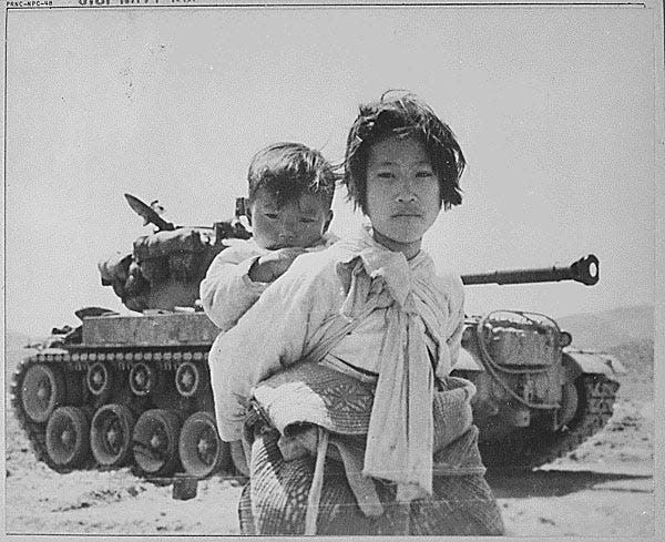A South Korean girl carries a baby near a tank in June 1951.