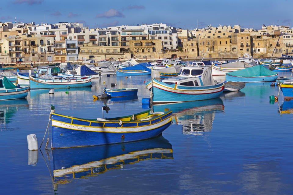 Traditional colourful Maltese fishing boats in St George's bay against blue skies in Birzebugga, Malta.