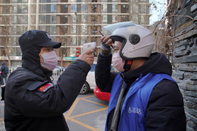 Security officer takes body temperature measurement of a delivery worker at a residential compound in Beijing