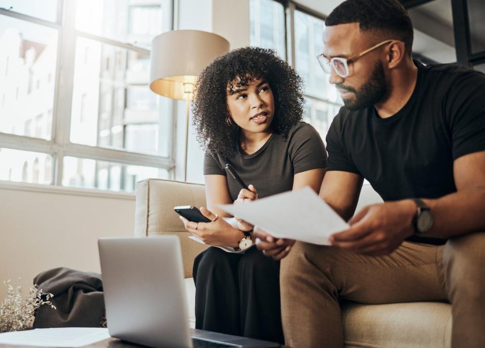 Two people sit on a couch and look at a document.