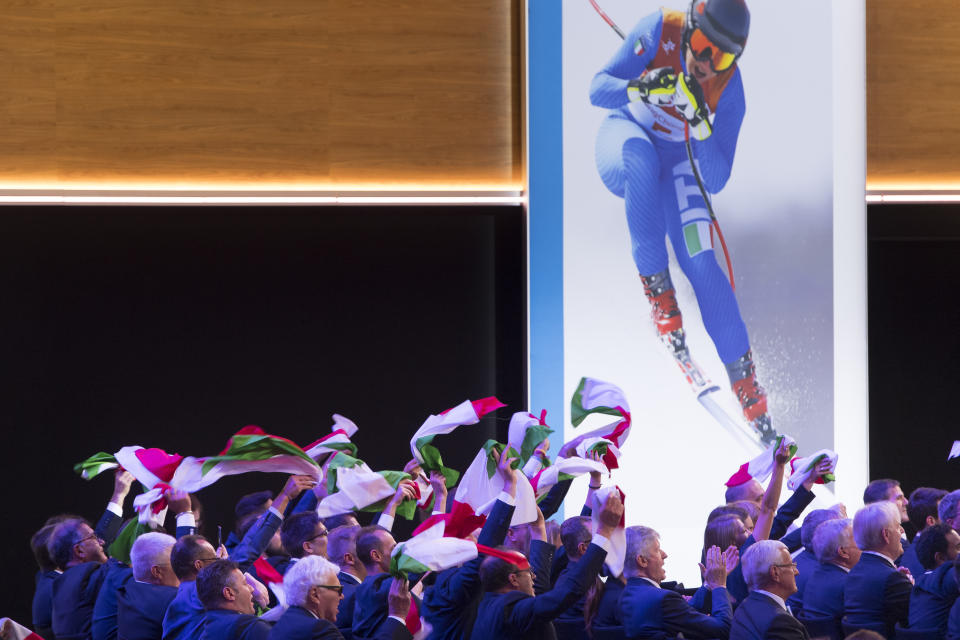 Italy members of delegation cheer with Italian flags during the final presentation of the Milan-Cortina candidate cities the first day of the 134th Session of the International Olympic Committee (IOC), at the SwissTech Convention Centre, in Lausanne, Switzerland, Monday, June 24, 2019. The host city of the 2026 Olympic Winter Games will be decided during the134th IOC Session. Stockholm-Are in Sweden and Milan-Cortina in Italy are the two candidate cities for the Olympic Winter Games 2026. (Laurent Gillieron/Keystone via AP)