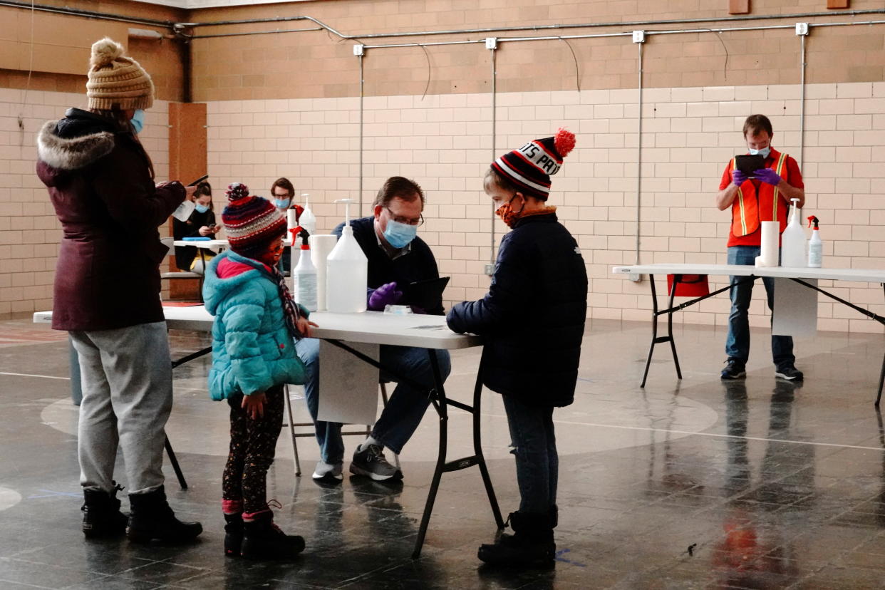 A family checks in on a tablet for self-administered COVID-19 saliva tests at a testing site.