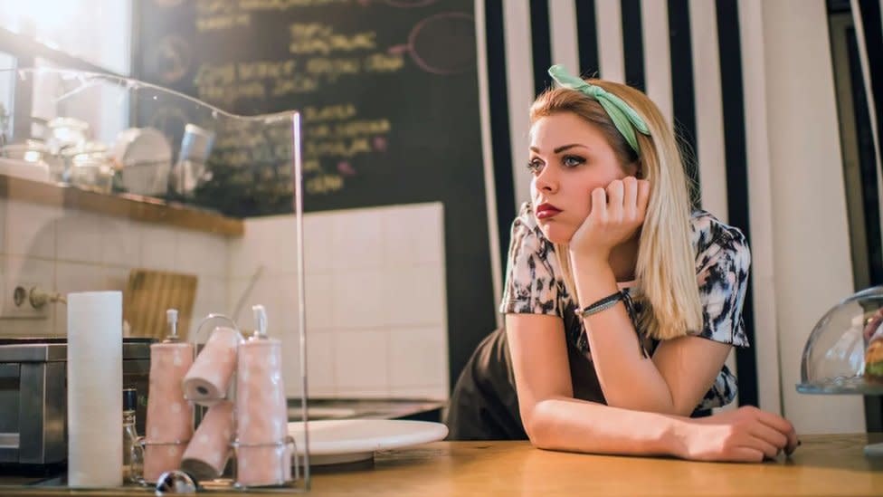 Una mujer con cara de aburrida frente a mostrador.