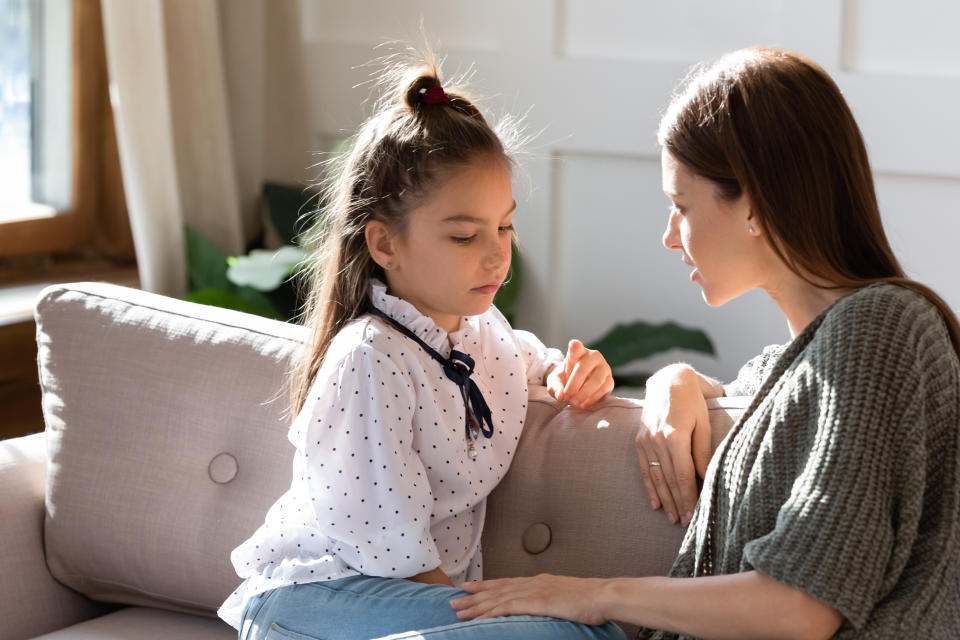 Upset small schoolgirl having trustful conversation with compassionate young mother, sitting together on sofa. Wise mommy comforting soothing little child daughter, overcoming problems at home.