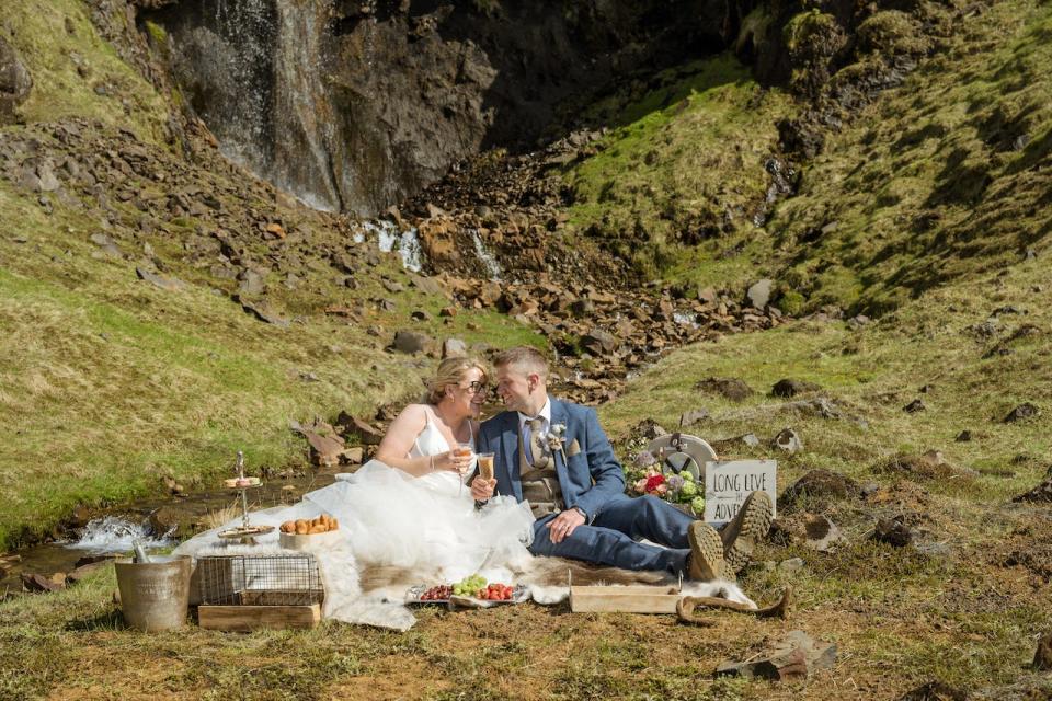 A bride and groom picnic in front of a waterfall in Iceland.