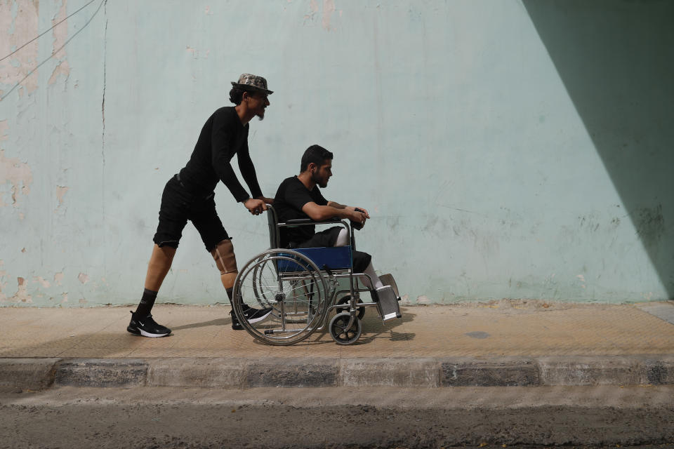 A Syrian soldier who lost his legs while fighting in Syria's war, helps his comrade after a physical therapy session, at the Ahmad Hamish Martyr hospital in Damascus, Syria Sunday, Oct. 7, 2018. (AP Photo/Hassan Ammar)