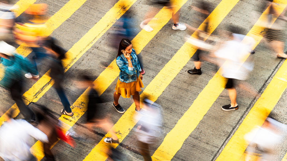 Motion blur as people cross the street at a zebra crossing, while a woman slowly walks, as she talks on the phone.