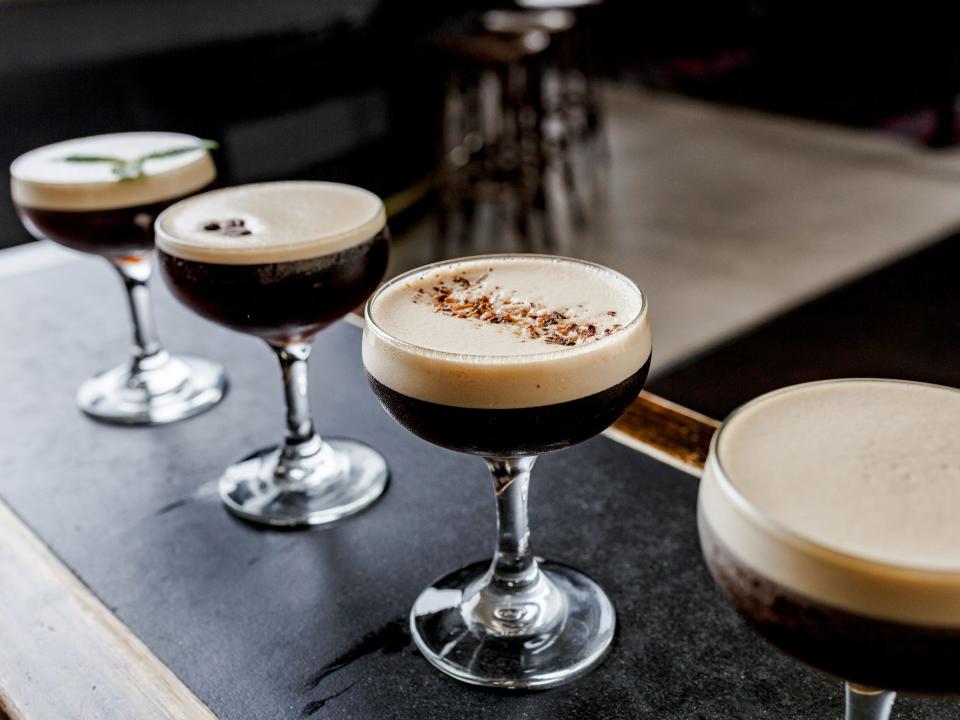 four espresso martinis with different garnishes lined up on a bar
