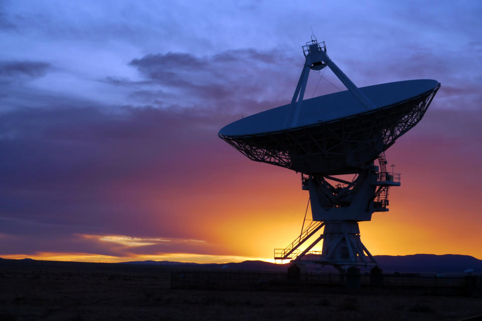 A satellite dish pointed up to space in front of a sunset.