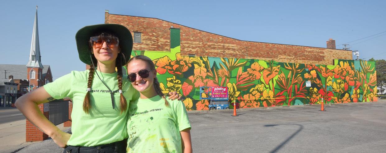 Artist George Rose of Austraila (left) with the help of artist Presley Bergmooser of Monroe painted the large abstract mural on the wall of Logan Charles Salon in downtown Monroe as part of the Plnting Seeds program. The abstract painting features the Michigan monkeyflower and the inland pigface flower from Australia.